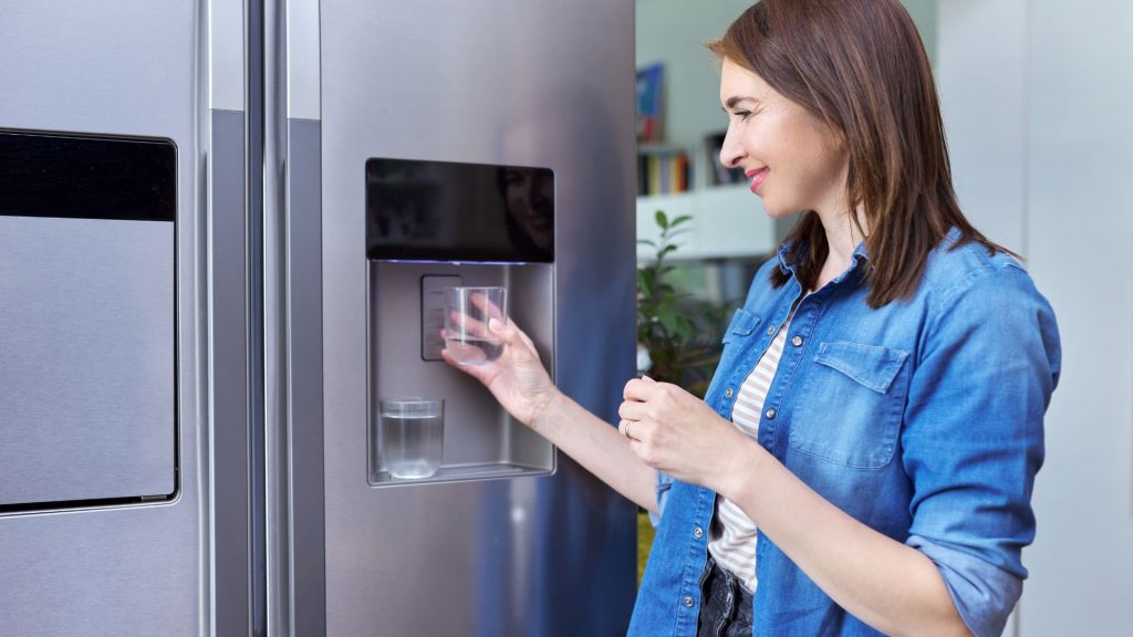 A lady gets water from her fridge after learning how to change fridge water filters.